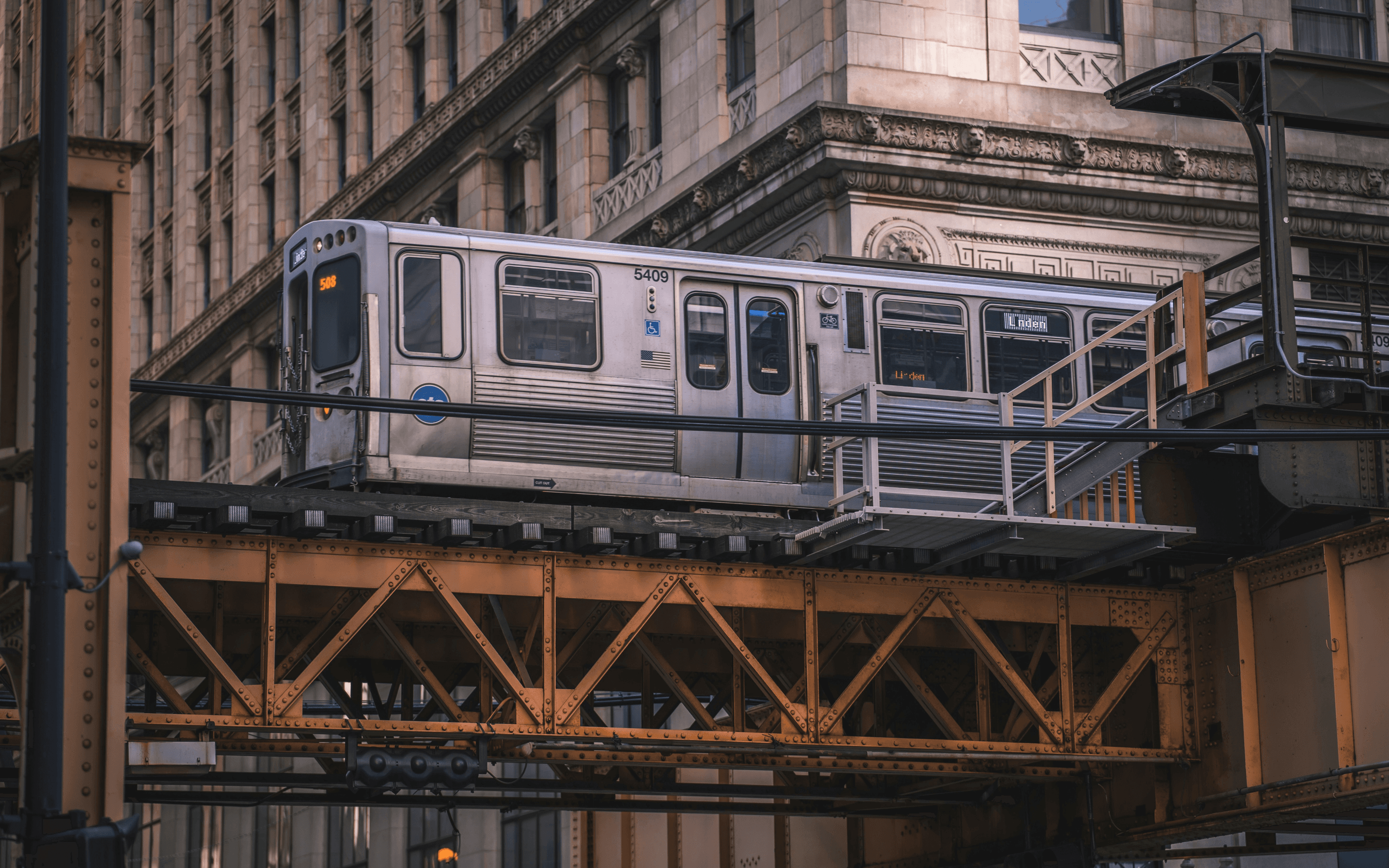 CTA L train traveling on an elevated track through Chicago's Loop, framed by historic Loop architecture and the steel bridge truss below